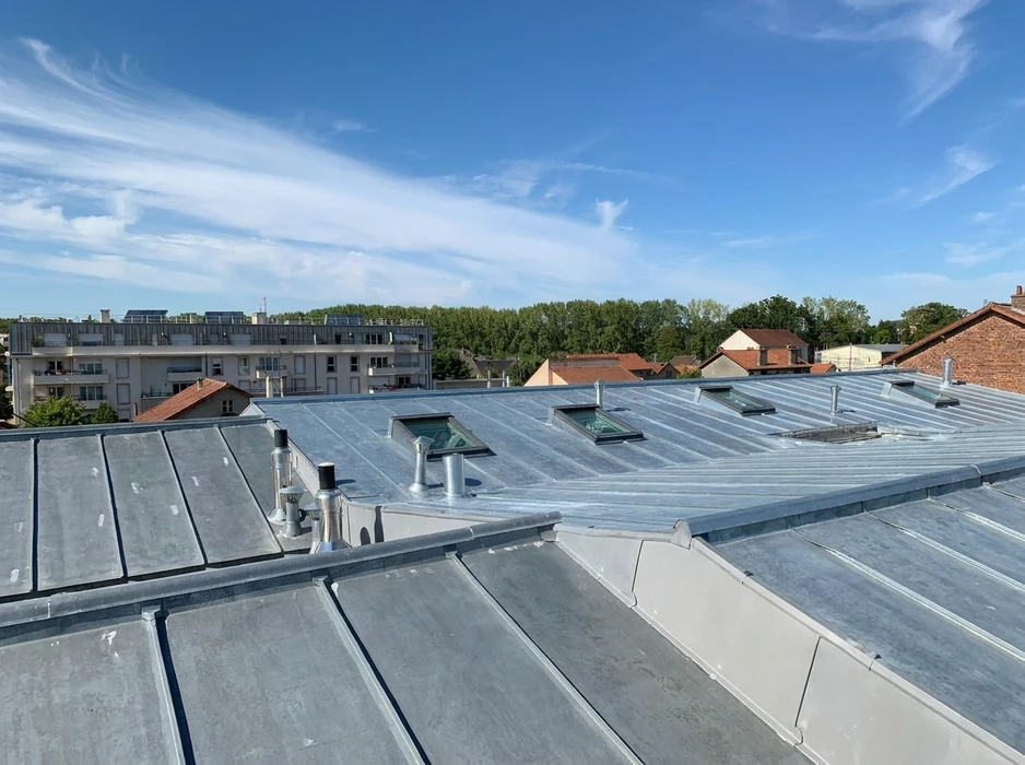 Toiture en zinc à joints debout vue en plongée, avec fenêtres de toit type Velux et sorties de ventilation en inox
