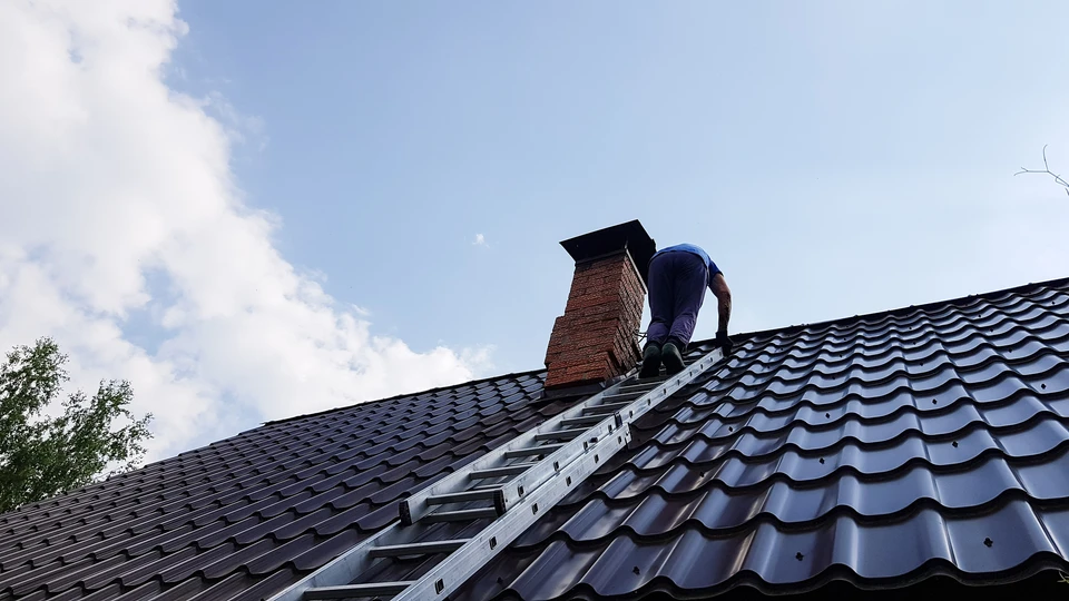 Couvreur professionnel travaillant sur toiture en tuiles métalliques, utilisant une échelle de toit pour accéder à une cheminée en briques