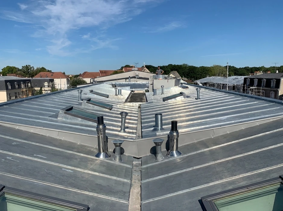 Toiture-terrasse en zinc à joint debout vue en plongée, avec un technicien debout en arrière-plan