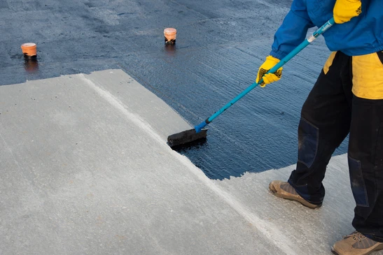 Ouvrier en tenue de protection applique un revêtement d'étanchéité bleu sur une toiture terrasse