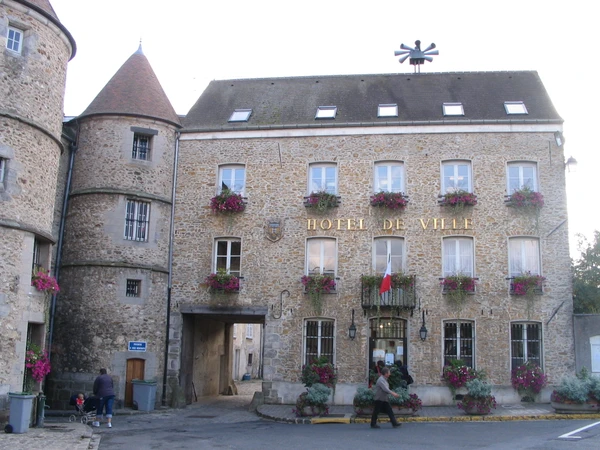 Photographie en jour clair d'une maison résidentielle typique de Seine-et-Marne à Tournan-en-Brie, dotée d'une toiture en bon état visible depuis la rue ou d'une légère perspective aérienne, montrant la façade et la couverture de la maison avec un arrière-plan de paysage rural ou de quartier résidentiel. La maison doit être représentative du secteur géographique couvert par G.M.C.