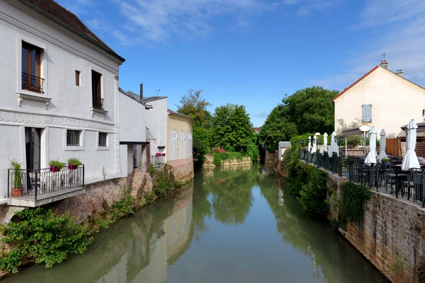 Photographie d'une maison ou d'un petit immeuble résidentiel typique à Coulommiers ou en Seine-et-Marne, prise de jour par beau temps. L'image doit montrer clairement la toiture et la structure de la couverture (visibles depuis un angle permettant de bien voir les tuiles, ardoises ou zinc), soit en perspective frontale avec légère vue de la toiture, soit en vue légèrement surélevée. L'arrière-plan doit montrer un environnement urbain ou péri-urbain du secteur (rue résidentielle, contexte local typique). La photo doit être nette, bien éclairée, sans texte ni logo visible.