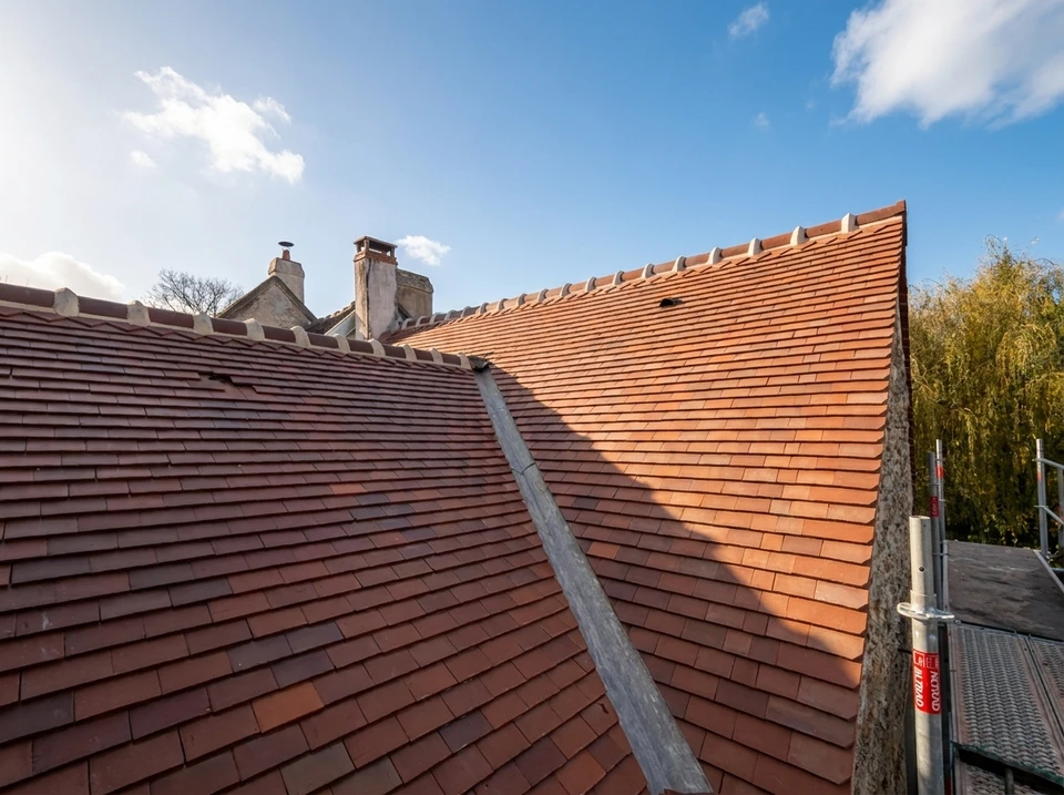 Chantier de toiture en cours avec ouvrier installant des tuiles plates grises sur charpente à structure métallique rouge